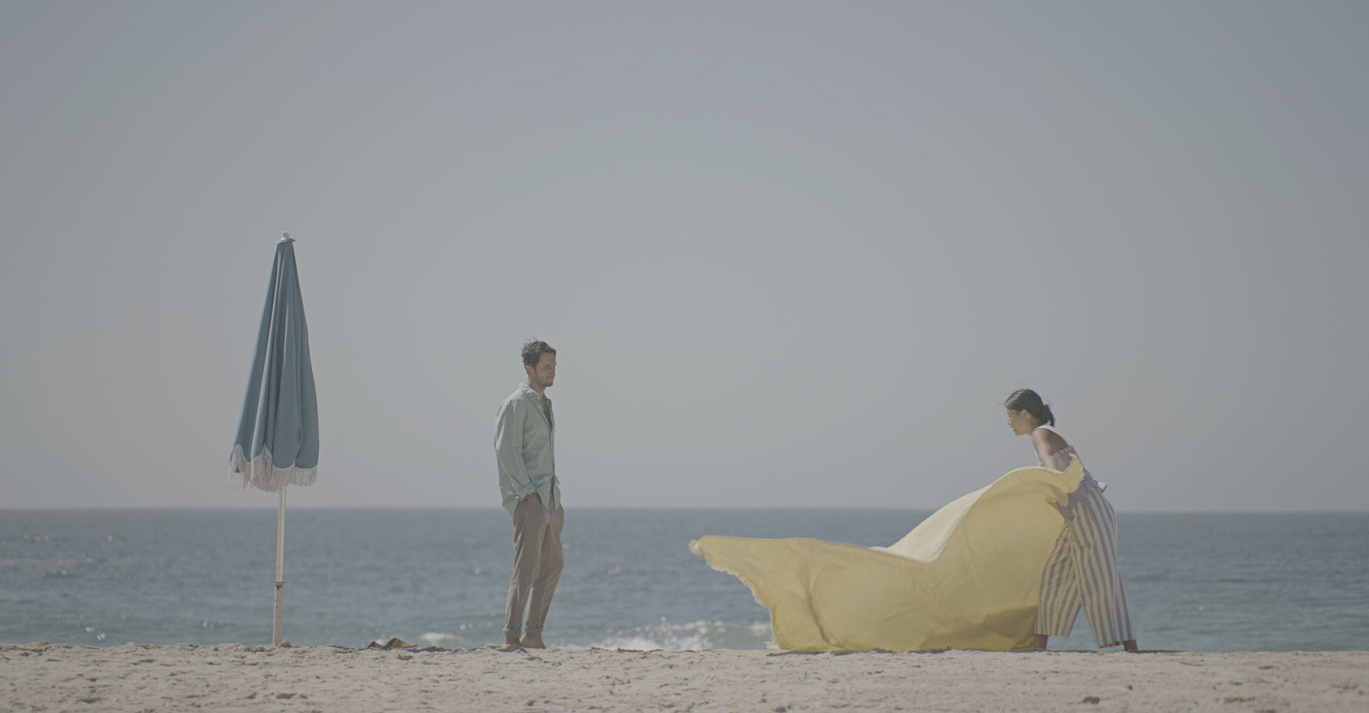 A man and woman setting a blanket on the beach.